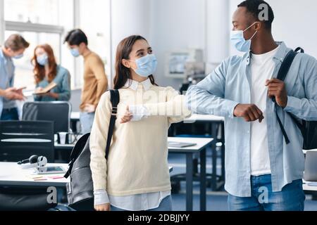 Multirassische Schüler tragen Gesichtsmasken Begrüßung und stoßen Ellbogen Stockfoto