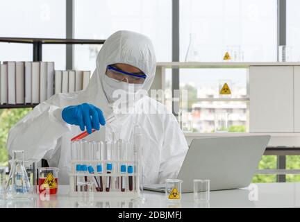 Epidemiologische Forscher in Virusschutzkleidung, die Chemikalien nach Formeln aus Computern mischt. Arbeitsatmosphäre in der Chemica Stockfoto