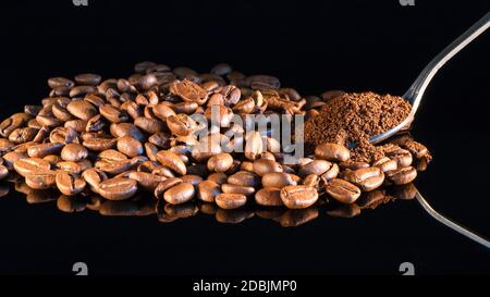 Kaffeebohnen auf schwarzem Spiegelhintergrund Nahaufnahme mit einem Löffel gemahlenen Kaffee. Stockfoto