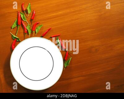 Weißer leerer Teller mit Chilischoten und Basilikum der Hintergrund ist echtes Massivholz. Food-Show-Konzept geeignet für die Werbung von Lebensmitteln und Display-Schilder. Stockfoto