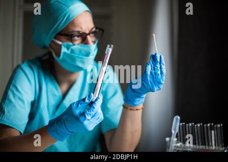 Konzeptionelle Aufnahme eines Arztes, der einen Reagenzglas hält und betrachtet, während er Proben auf Vorhandensein von Coronavirus testet (COVID-19). Stockfoto