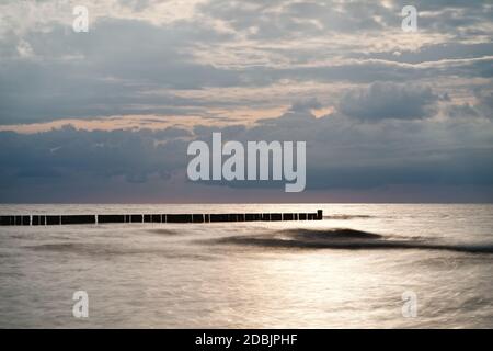 Ruhiger Strandaufnahme der Ostseeküste mit einer Reihe von Groynes parallel zum Horizont, davor eine markante Welle, die Wasseroberfläche ist geglättet Stockfoto