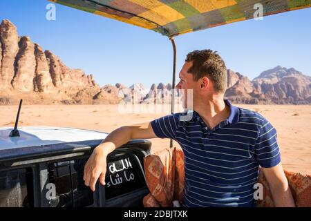 Ein Mann fährt auf einem LKW durch die Wüste des Wadi Rum in Jordanien, Berge im Hintergrund. Stockfoto