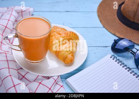 Milchtee in Gläsern und Vollkornbrot mit Notizbuch und Sonnenbrille. Es gibt einen Strand auf dem blauen Holztisch des Patels. Urlaub Milch Tee rela Stockfoto