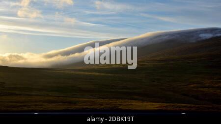 Eine Hochsommernacht in Island. Wolken treiben einen Berg hinunter. Contre-jour. Stockfoto