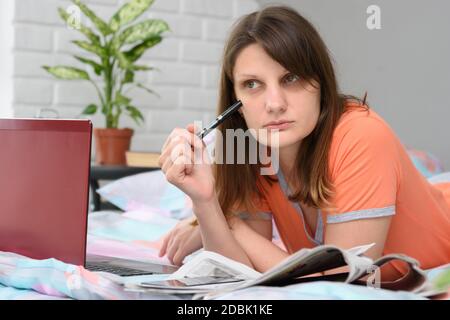 Das Mädchen dachte, während sie vor einem Laptop auf der Suche nach Arbeit lag Stockfoto