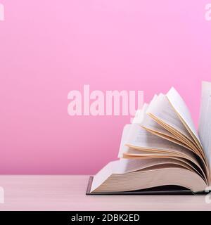 Ein großes, dickes Hardcover-Buch liegt auf einem Tisch aus hellem Holz. Das Buch ist offen, die Blätter der Seite sind ausgefächert, und das Rosa ist ein schwarzer Hintergrund Stockfoto