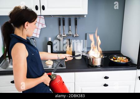 Frau mit Feuerlöscher zu stoppen Feuer zum Brennen von kochenden Topf in der Küche Stockfoto