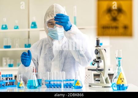 Wissenschaftler halten Reagenzglas und untersuchen für seine Forschung und entwickeln Impfstoff gegen Coronavirus covid-19 Pandemie im Laborraum mit Vorsicht Beschilderung. Stockfoto