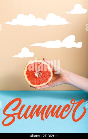 Beschnittene Ansicht der Frau, die saftige Hälfte der Grapefruit in der Nähe hält Sommer-Schriftzug auf beige und blau Stockfoto