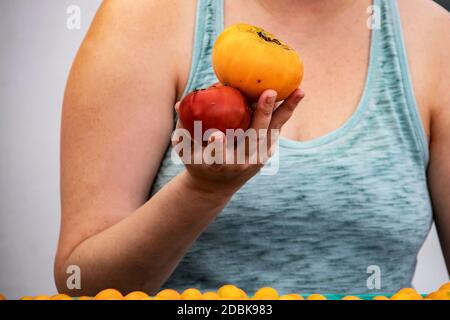 Nahaufnahme der Frau in Tank Top hält zwei Erbstück Tomaten In ihrer Hand auf dem Bauernmarkt - nicht erkennbar Stockfoto