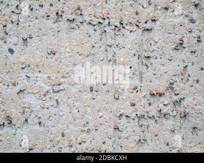 Formatfüllende Ansicht einer grob verputzten grauen Wand mit groben Kieselsteinen. Stockfoto