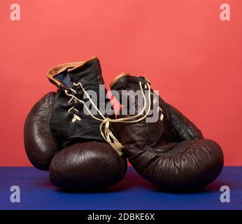 Braune Leder Vintage Boxhandschuhe auf rotem Hintergrund, Sportausrüstung Stockfoto
