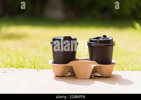Nahaufnahme von zwei schwarzen Pappbecher heißen Kaffee zum Mitnehmen auf dem Boden außerhalb des Cafés auf dem Garten Platz der grünen Blätter Farbe Hintergrund für Kopie sp Stockfoto