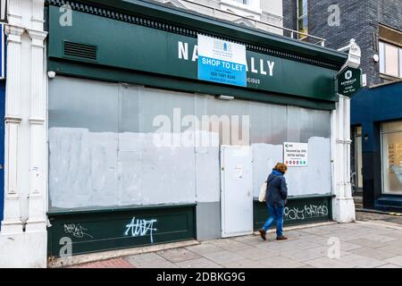 Eine Frau läuft an einem leeren und verschlossenen Laden in Kentish Town, London, vorbei Stockfoto