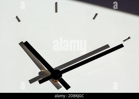 Die Hände der Wanduhr, mit den Schatten auf der weißen, zementartigen Hintergrundstruktur. Der Schatten im oberen Teil des Bildes Stockfoto