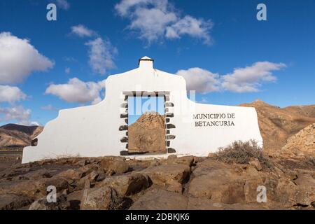 Typisches Gemeindeschild (weißes Bogentor) in der Nähe von Betancuria Dorf mit Wüste Berglandschaft im Hintergrund, Fuerteventura, Kanarische Inseln, S Stockfoto