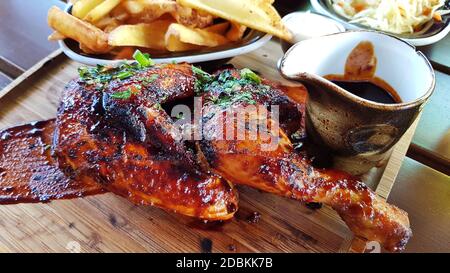 Die Hälfte des gebratenen Hähnchens wird auf einem Holztablett serviert. Auf einem Tablett frittierte Kartoffeln und Soße. Fein gehackte grüne Zwiebeln auf gebratenem Huhn. Stockfoto