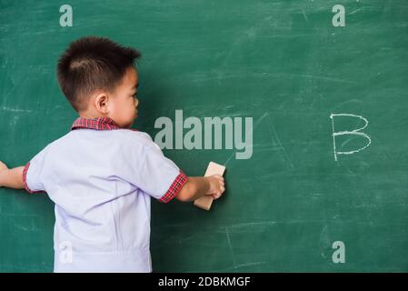 Zurück zur Schule. Zurück von asiatischen niedlichen kleinen Kind junge Kindergarten Vorschule in Schüler Uniform wischen sauber oder löschen Kreide auf grünen Schule Tafel w Stockfoto