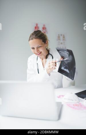 Hübsche und junge Ärztin diskutiert Röntgenbild online mit ihrem Patienten Stockfoto