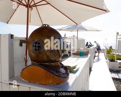 Russland, Sotschi 31.10.2020. Dekorativer Tauchhelm aus Bronze steht auf einer weißen Holzstange unter einem Sonnenschirm am Strand Stockfoto