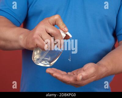 Mann in einem blauen T-Shirt hält einen transparenten Plastikbehälter mit einem Handdesinfektionsmittel und drückt ihn aus der Flasche Stockfoto