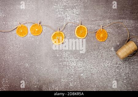 Kreative Girlande aus hausgemachten getrockneten Orangen Scheiben mit Wäscheklammern auf Hanfseil. Weihnachten und Neujahr, Winter Komposition. Draufsicht, flach liegend Stockfoto
