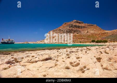 2019, 4. JUNI: - GRIECHENLAND, DIE INSEL KRETA, BALOS - die Burg auf dem Gipfel des Berges und die Menschen am Strand darunter. Stockfoto