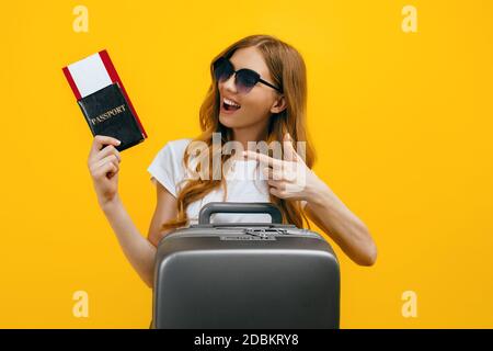 Glückliche schöne Frau, Mädchen mit einem Koffer und Reisepass mit Tickets auf einem gelben Hintergrund. Das Konzept von Reisen, Business Stockfoto