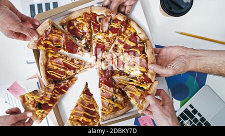 Leute, die Pizza zum Mittagessen im Creative Office einnehmen. Verschiedene Hände Nehmen Pizza. Essen am Arbeitsplatz. Fast Food Stockfoto