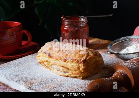 Fresh Puff mit Pflaume oder rote Johannisbeere Marmelade auf dem Tisch mit einer roten Tasse und Glas Marmelade auf dem schwarzen Hintergrund besetzt. Stockfoto