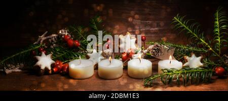 Drei angezündete kleine Kerzen für den dritten Advent mit Weihnachtsdekoration auf dunklem rustikalem Holz, Panoramaformat, Kopierraum, ausgewählter Fokus Stockfoto