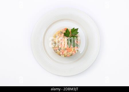 Russischer traditioneller Salat Olivier mit Petersilie auf einem weißen Teller auf weißem Hintergrund Draufsicht. Konzept des Neujahrsmenüs. Kopie des Speicherplatzes. Isoliert Stockfoto