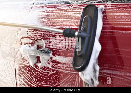 Rotes Auto gewaschen in selbst dienen Autowäsche, Detail auf Bürste verlassen Striche an Seitentür und Griff. Stockfoto