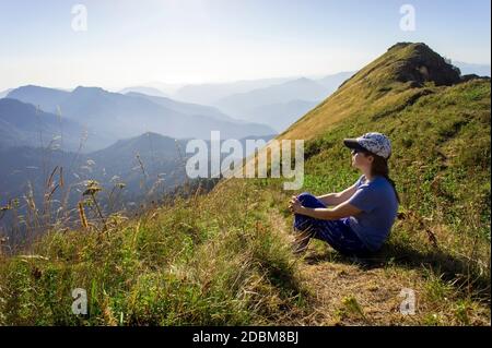 Junge Frau in einer Mütze sitzt zwischen den Bergen und Blick auf die untergehende Sonne und Bergblick. Landschaft, Aibga Kamm, Wanderung und Trekking, Reisen a Stockfoto