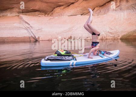 Frau in Kopfstand-Position auf dem Paddelbrett, Lake Powell, Utah, USA Stockfoto