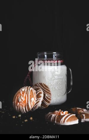 Ein Glas Milch mit einem Weihnachtsband und einem Plätzchen mit Orangenmarmelade verziert. Fokus auf Milch, selektiver Fokus, geringe Schärfentiefe Stockfoto