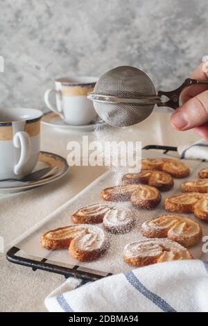 Eine Dame streut Zuckerpulver von einem Sprinkler auf die Kekse. Kekse mit Puderzucker. Stockfoto