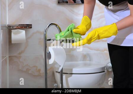 Damenhände in Gummischutzhandschuhen wischen den Toilettenpapierständer ab. Nicht erkennbares Foto. Sauberkeit und Hygiene im Bad. Speicherplatz kopieren. Stockfoto