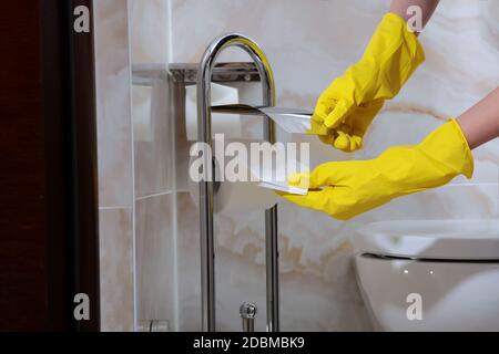 Damenhände in Gummischutzhandschuhen wischen den Toilettenpapierständer ab. Foto ohne Gesicht, nur Hände. Sauberkeit und Hygiene im Bad. Kopieren Stockfoto