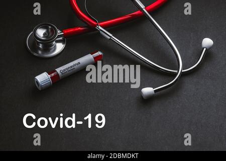 COVID-19-Text mit Stethoskop und Blutprobenvakuumschlauch auf schwarzem Hintergrund. Covid oder Coronavirus Konzept Stockfoto