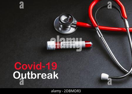 COVID-19-AUSBRUCHSTEXT mit Stethoskop und Blutprobenvakuumschlauch auf schwarzem Hintergrund. Covid oder Coronavirus Konzept Stockfoto