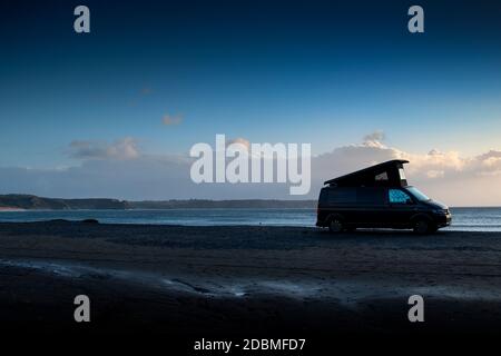 Ein VW T5 Wohnmobil mit Dach tauchte am Oxwich Bay Strand auf, Gower mit drei Klippen Bay & die Gower Landschaft im Hintergrund, wildes Campen in wales. Stockfoto