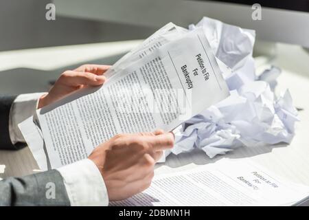 Beschnittene Ansicht des Geschäftsmannes, der Petition für Bankrott nahe Stapel hält Von zerbröckeltem Papier auf verschwommenem Hintergrund Stockfoto