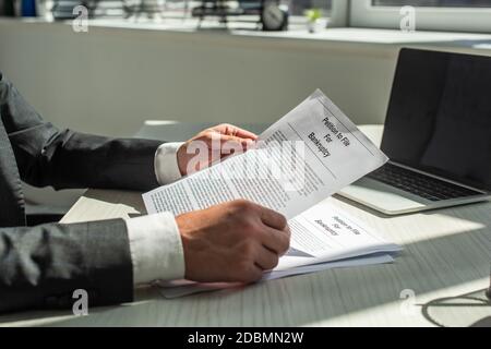 Beschnittene Ansicht des Geschäftsmannes, der Petition für Bankrott hält, während er am Arbeitsplatz auf verschwommenem Hintergrund sitzt Stockfoto