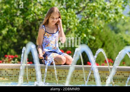 Ein Mädchen sitzt am Brunnen und schaut auf die Wasserstrahlen Stockfoto