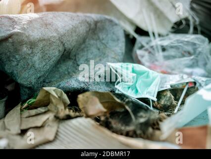 Gebrauchte Gesichtsmaske entsorgen im Hausmüll. Entsorgung von medizinischem Abfall mit unhygienischer Entsorgung. Kontaminierter Abfall in der Gemeinschaft. Einweg-Ohrbügel fa Stockfoto