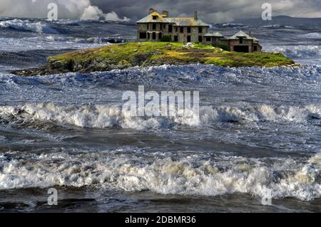 Dieses Fantasiebild einer gruseligen Insel und eines Hauses bei wildem Wetter basiert auf Craig y Mor in Trearddur Bay auf Holy Island, Anglesey, Nordwales. Stockfoto