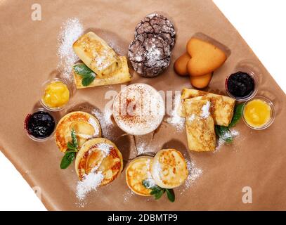 Zimtkaffee, verschiedene Marmeladen und hausgemachte Kekse, Strudel und Käse. Handgemachte Desserts und Kaffee in Papiertasse auf braunem Hintergrund. Oben Stockfoto