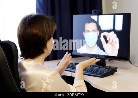 Online-Beratung mit einem Arzt, Frau hört sich die Arzt Empfehlungen sitzen vor der PC-Webcam. Mann in medizinischer Maske mit Pille Stockfoto